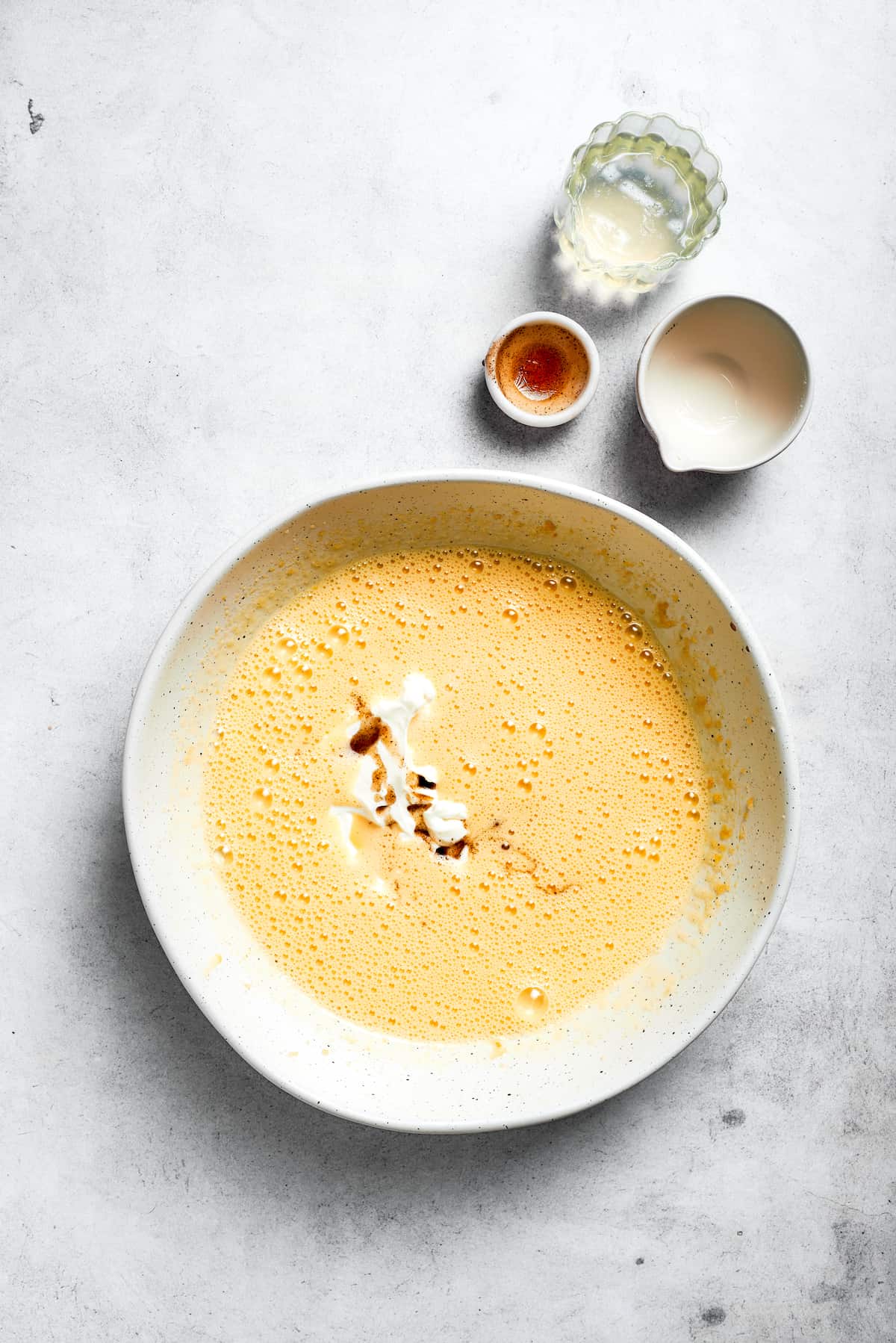 Buttermilk, sour cream, pineapple juice, and vanilla extract are added to the wet mixture in a bowl, ready to be combined.