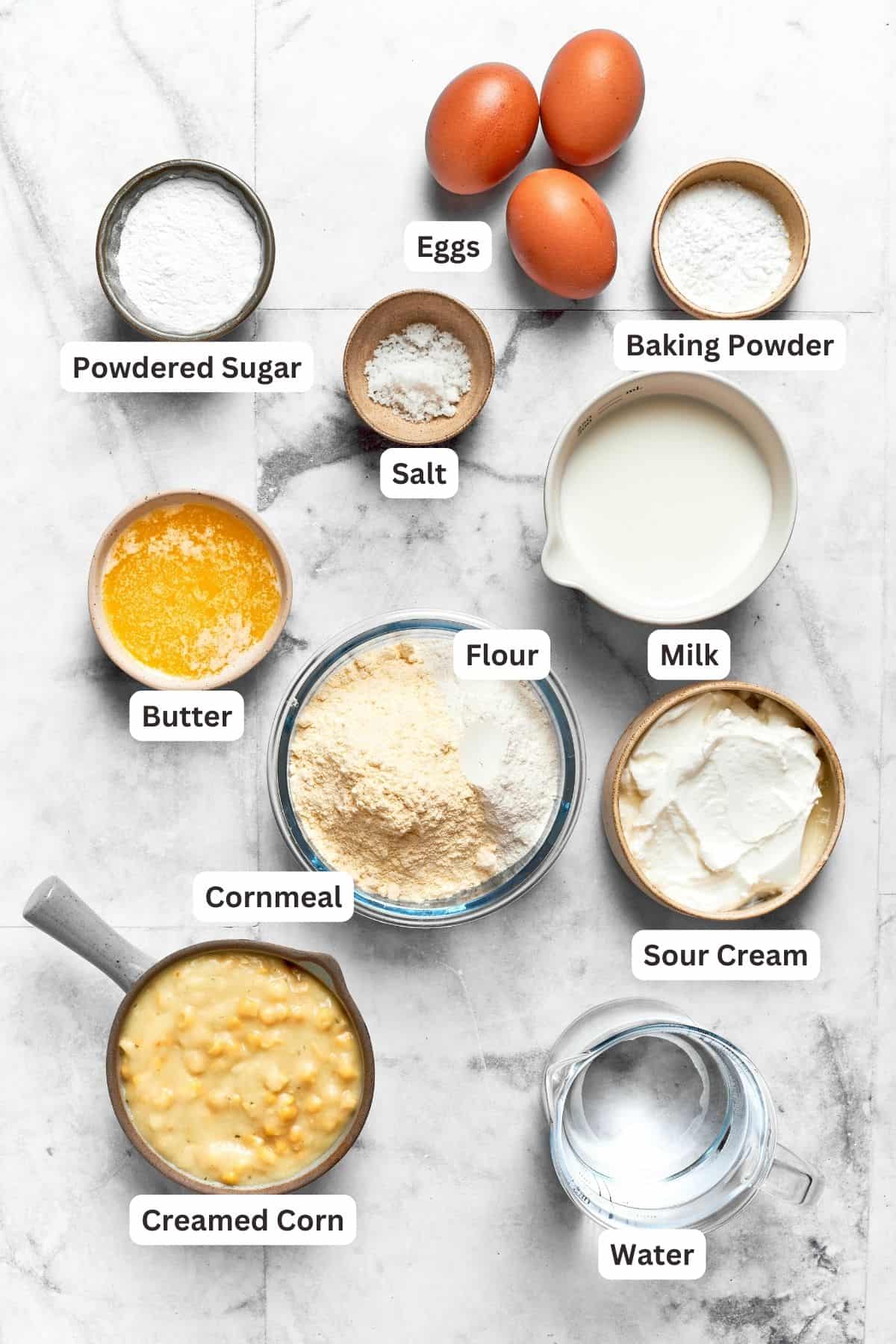 Ingredients needed for spoon bread are shown: baking powder, flour, cornmeal, butter, creamed corn, eggs, powdered sugar, water.
