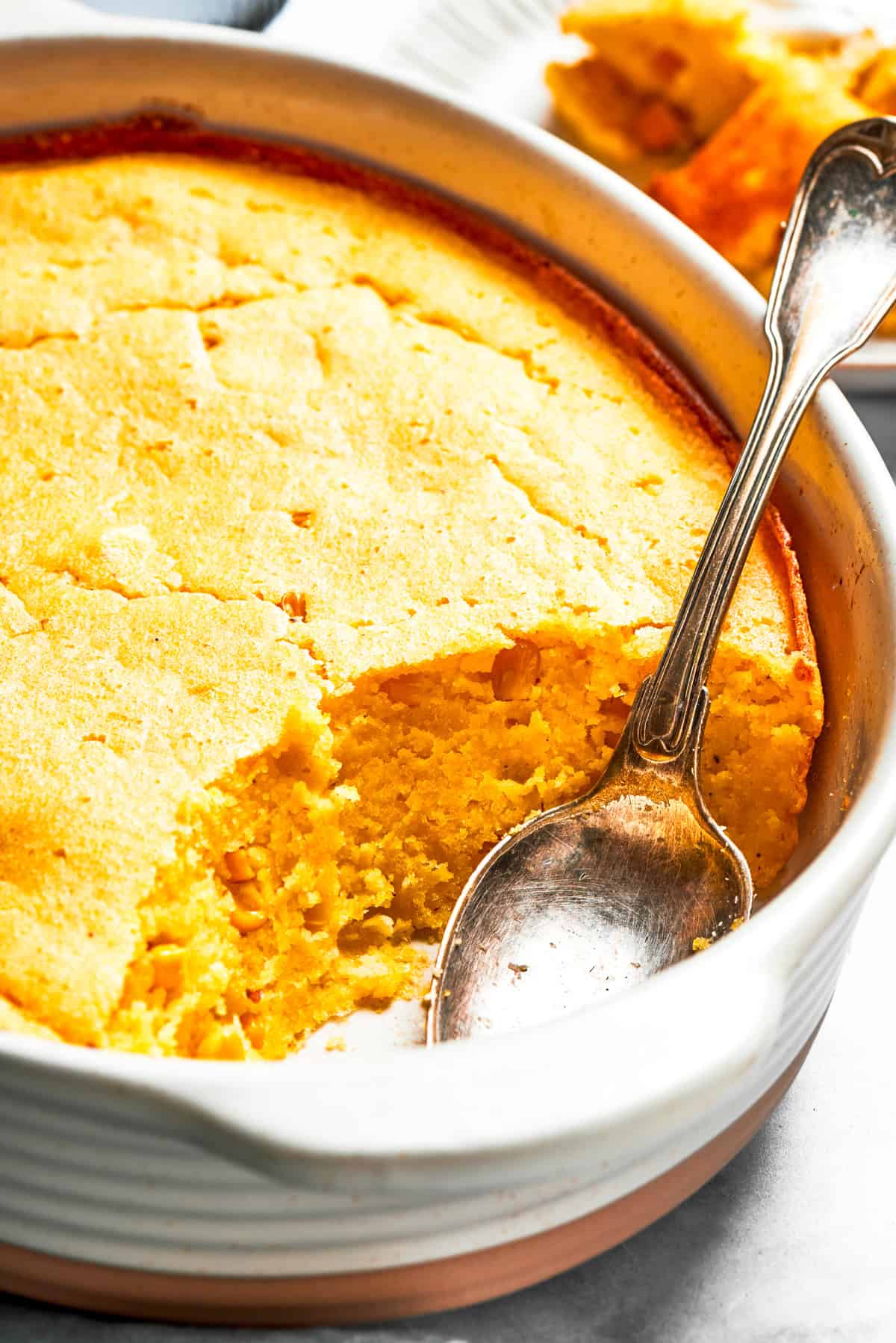 Spoon bread in a casserole dish with a spoon placed inside it.