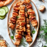 A platter of grilled chicken souvlaki on skewers surrounded by herbs and cucumber slices.