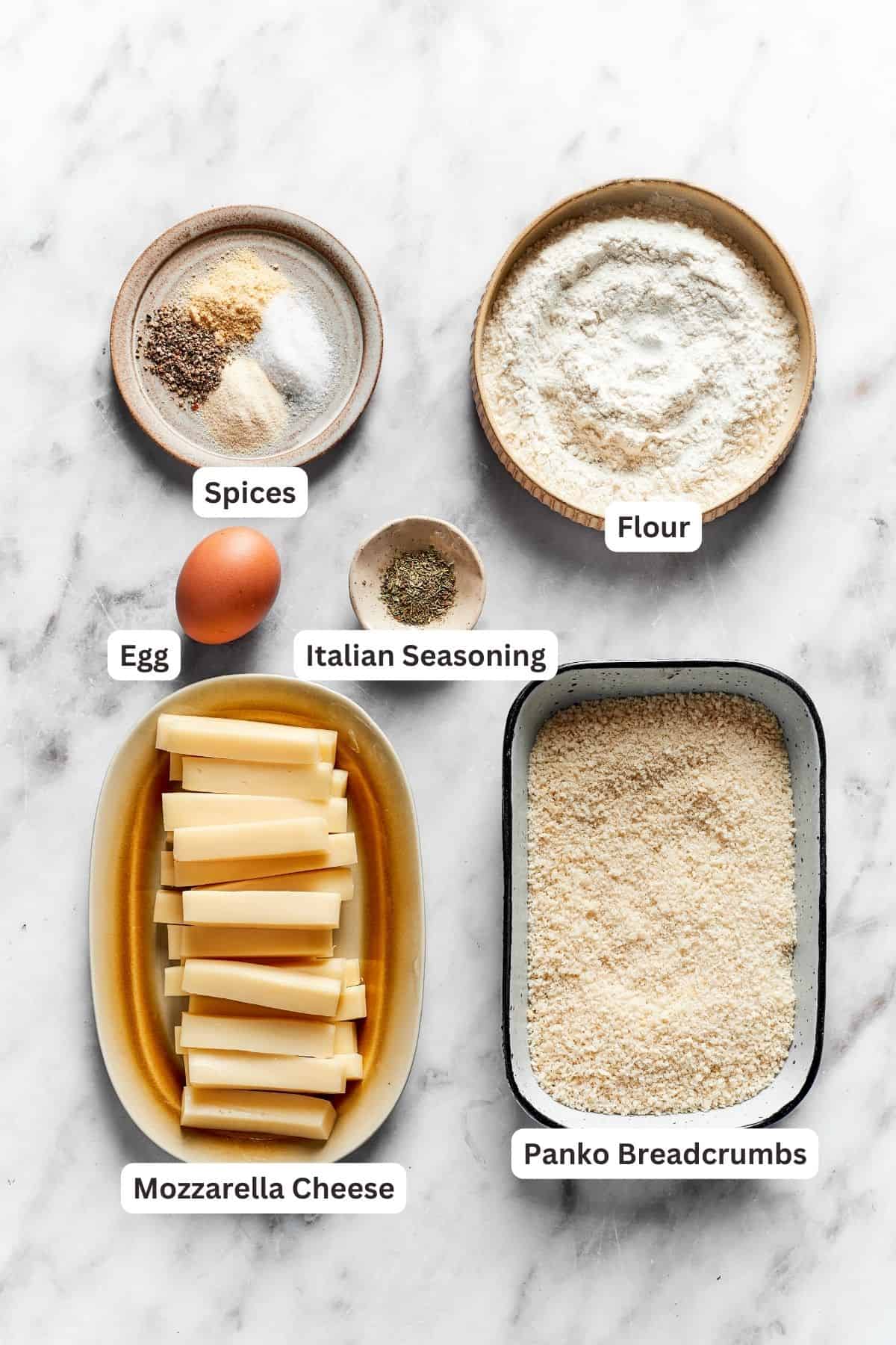 The ingredients for mozzarella sticks are shown portioned out and labeled: mozzarella cheese, panko breadcrumbs, flour, egg, Italian seasoning, salt and pepper.