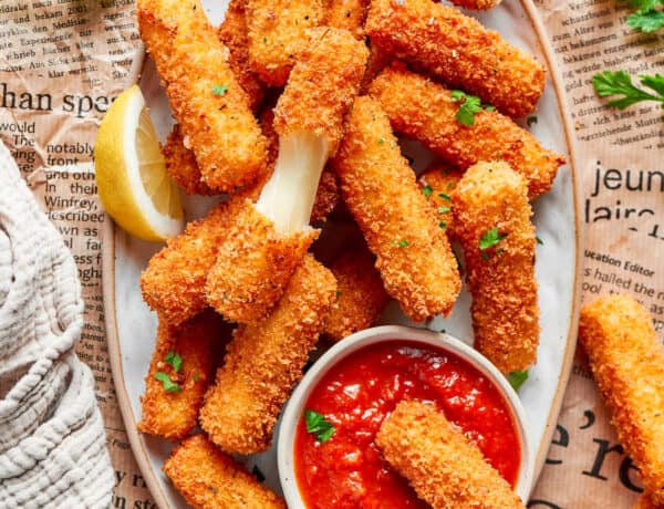 A platter of mozzarella sticks with one cut in half and one dipped in tomato sauce.
