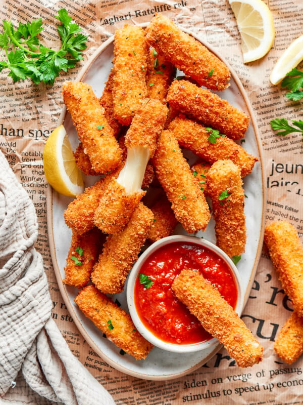 A platter of mozzarella sticks with one cut in half and one dipped in tomato sauce.