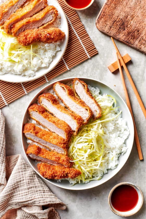Japanese Tonkatsu sliced and served over cabbage and rice on dinner plates.
