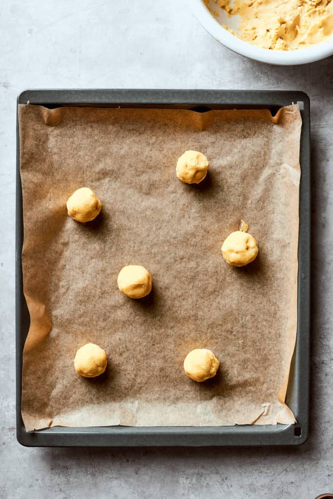 A lined baking sheet with balls of white chocolate chip cookie dough.