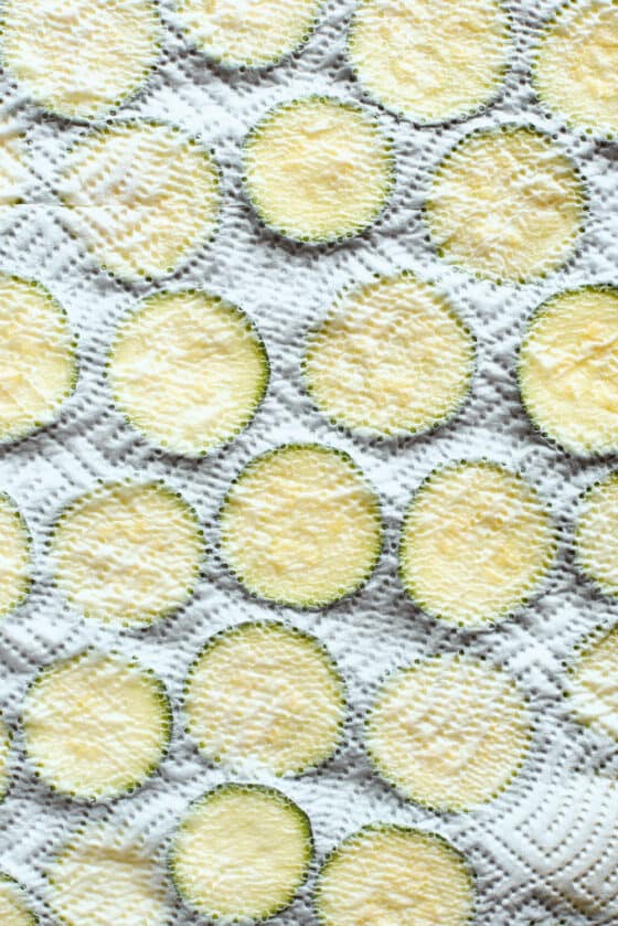 A paper towel covers a baking sheet of zucchini slices.