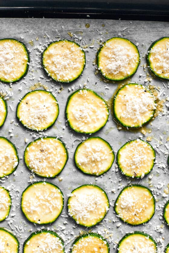The zucchini chips are spread out on a lined baking sheet.