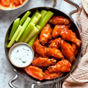A view of a table holding a towel and a pan with buffalo wings, sauce, and celery.