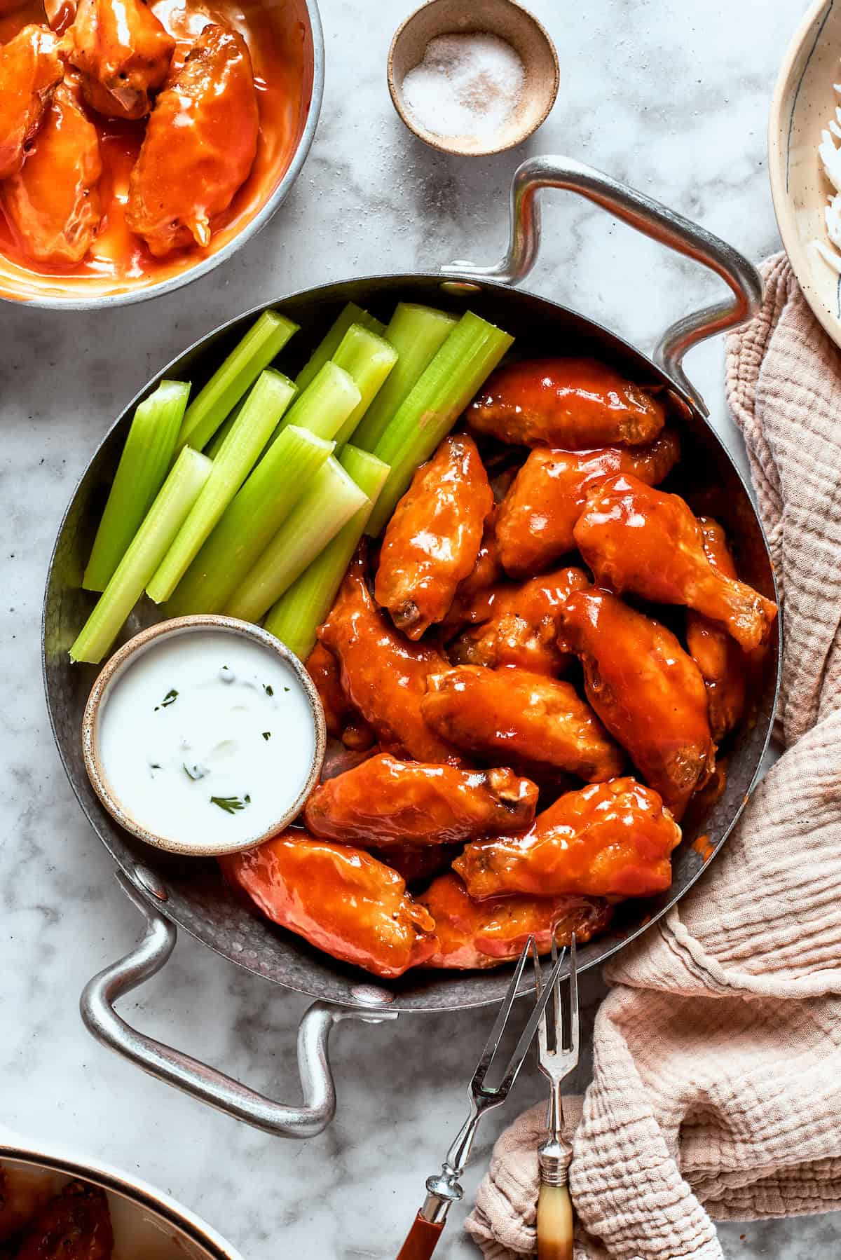 A view of a table holding a towel and a pan with buffalo wings, sauce, and celery.