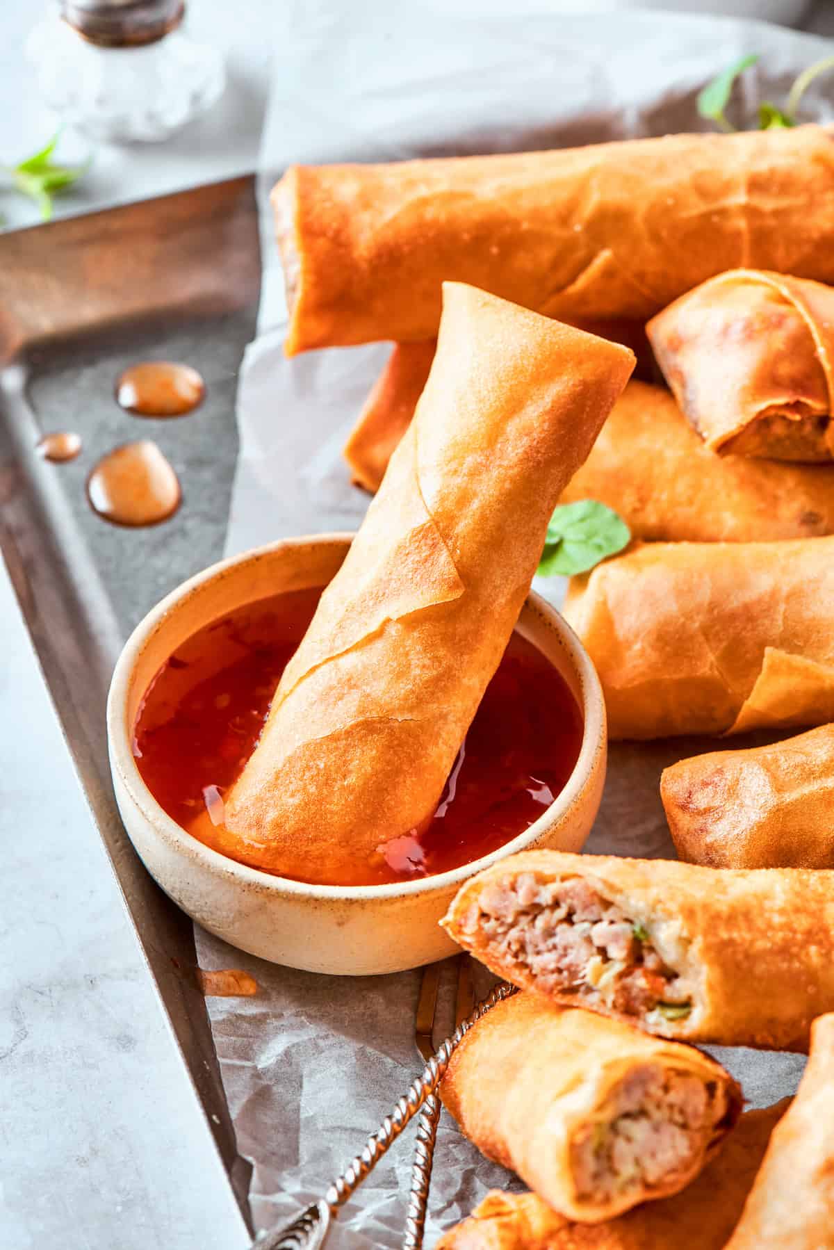 Sliced chicken egg rolls and whole egg rolls are served with a bowl of sauce, with one egg roll dipped in it.