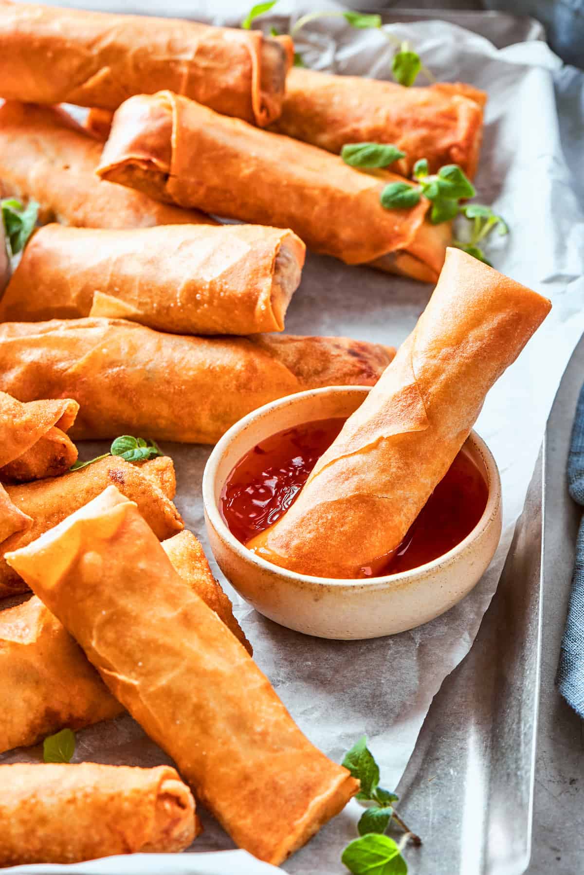 A chicken egg roll is dipped into sauce while other rolls lie around it.