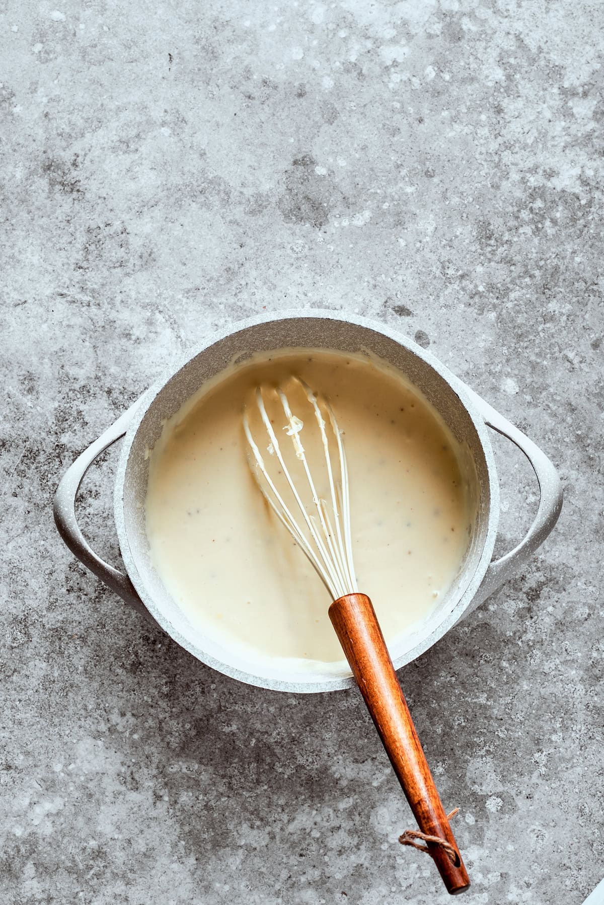 A whisk blends the sauce in a bowl.