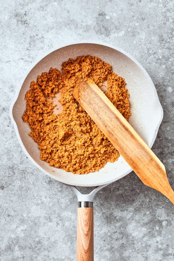 A wooden spoon mixes up the breadcrumbs in a pan.
