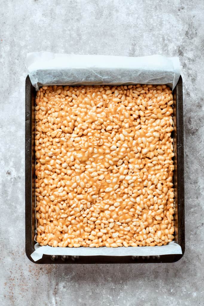 The rice crispy treat base is pressed into a pan.