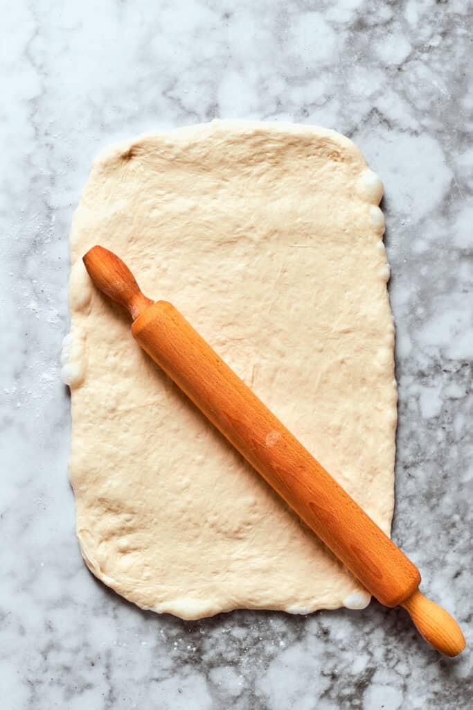 The pizza dough is rolled out with a rolling pin.
