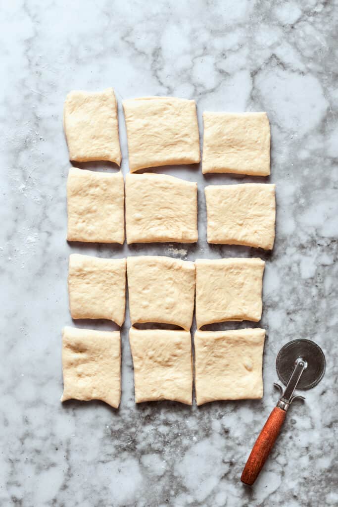 The pizza dough is cut into 12 squares.