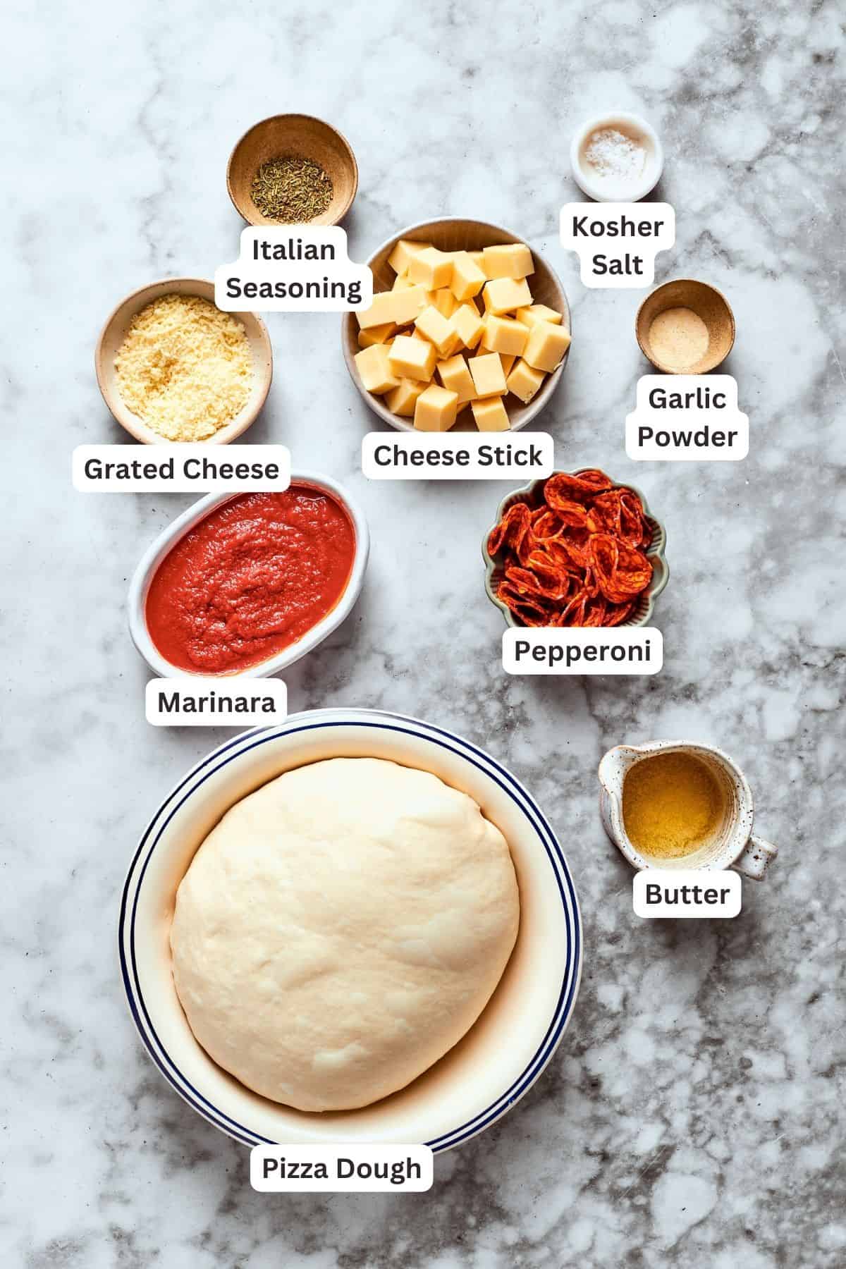 Ingredients for pizza burgers are labelled and portioned out: pizza dough, grated cheese, Italian seasoning, marinara sauce, pepperoni, butter, garlic powder, cheese stick, salt.