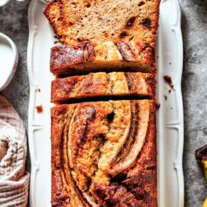 Sour cream banana bread in a loaf pan with bananas and other ingredients around it.