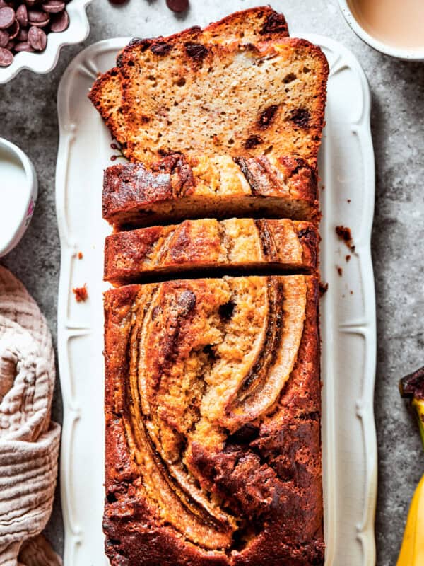 Sour cream banana bread in a loaf pan with bananas and other ingredients around it.