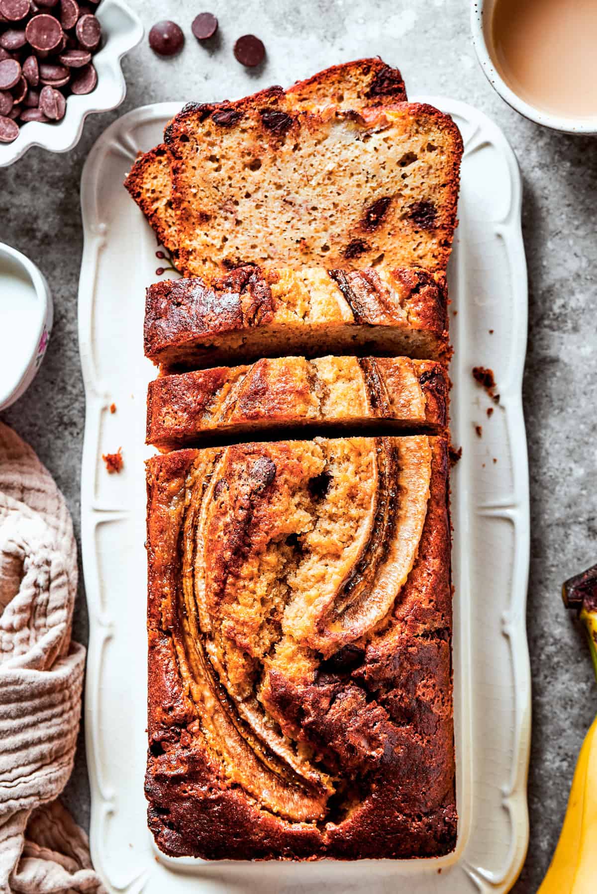 Sour cream banana bread in a loaf pan with bananas and other ingredients around it.