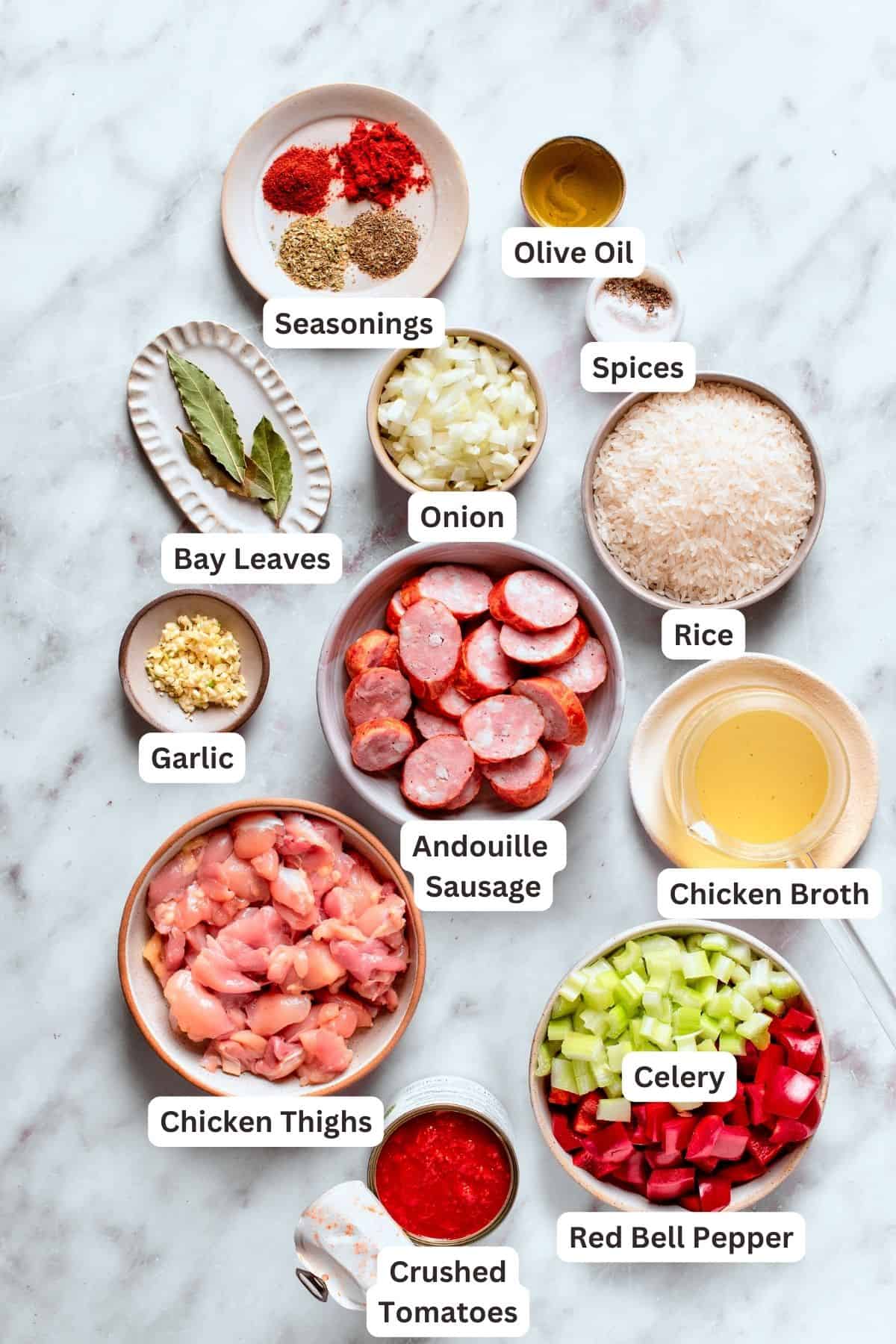 Chicken and sausage jambalaya ingredients are shown labeled: sausage, chicken, rice, garlic, chicken broth, seasonings, spices, olive oil, celery, red bell pepper.