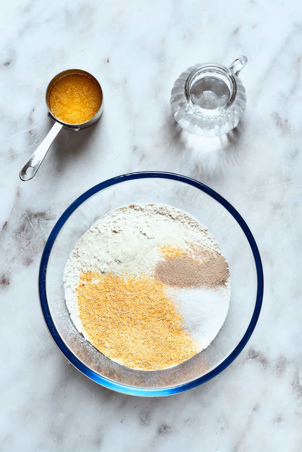 The dry ingredients for deep dish pizza crust, including flour, cornmeal, yeast, sugar, and salt, in a mixing bowl.
