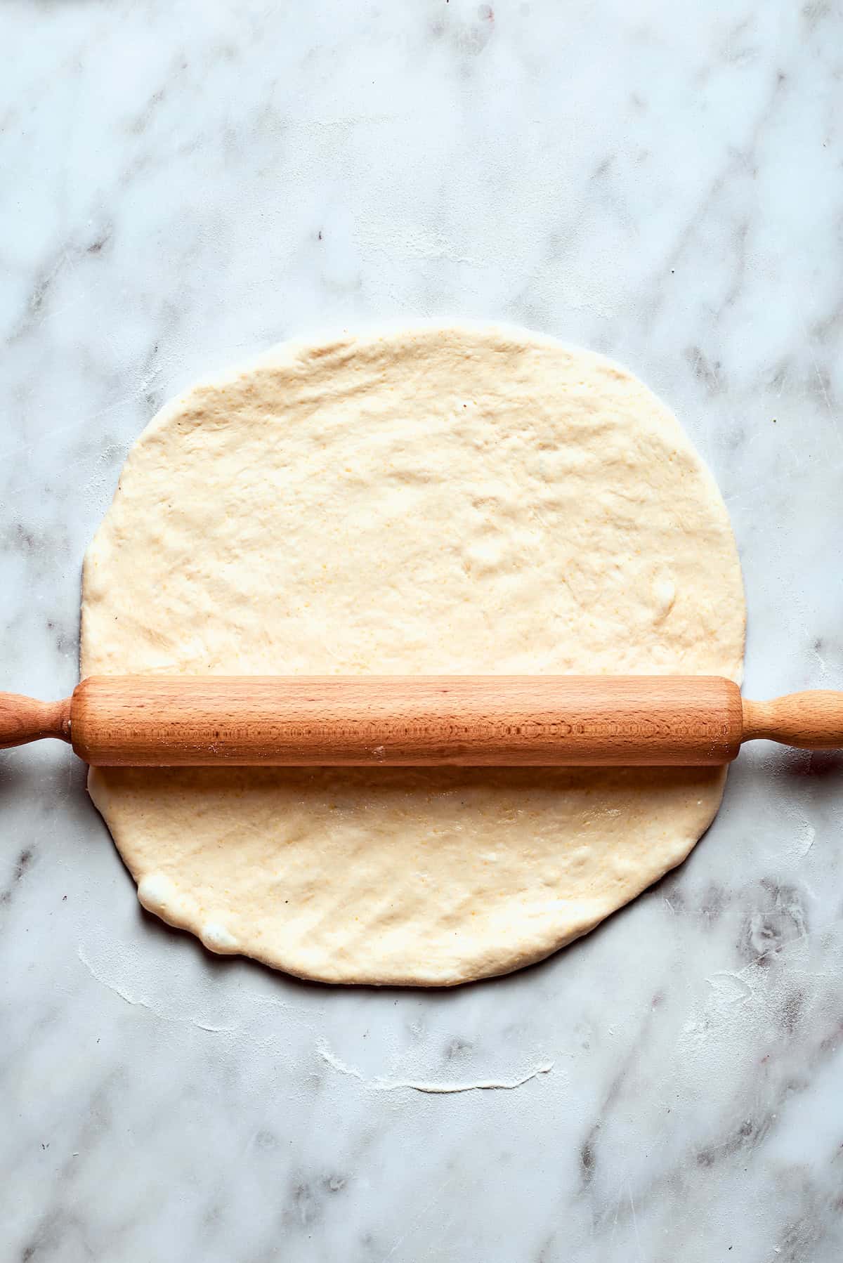 A rolling pin is used to flatten the deep dish pizza dough on a lightly floured surface.