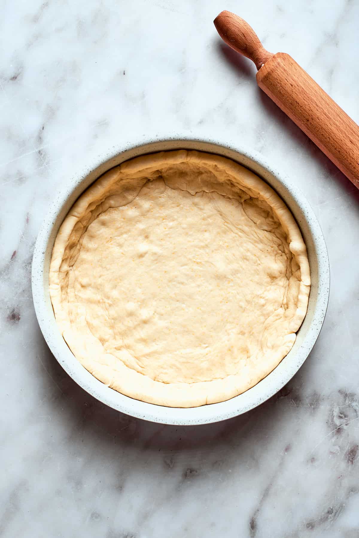 The pizza dough is carefully pressed into a deep-sided baking pan, covering the bottom and sides.