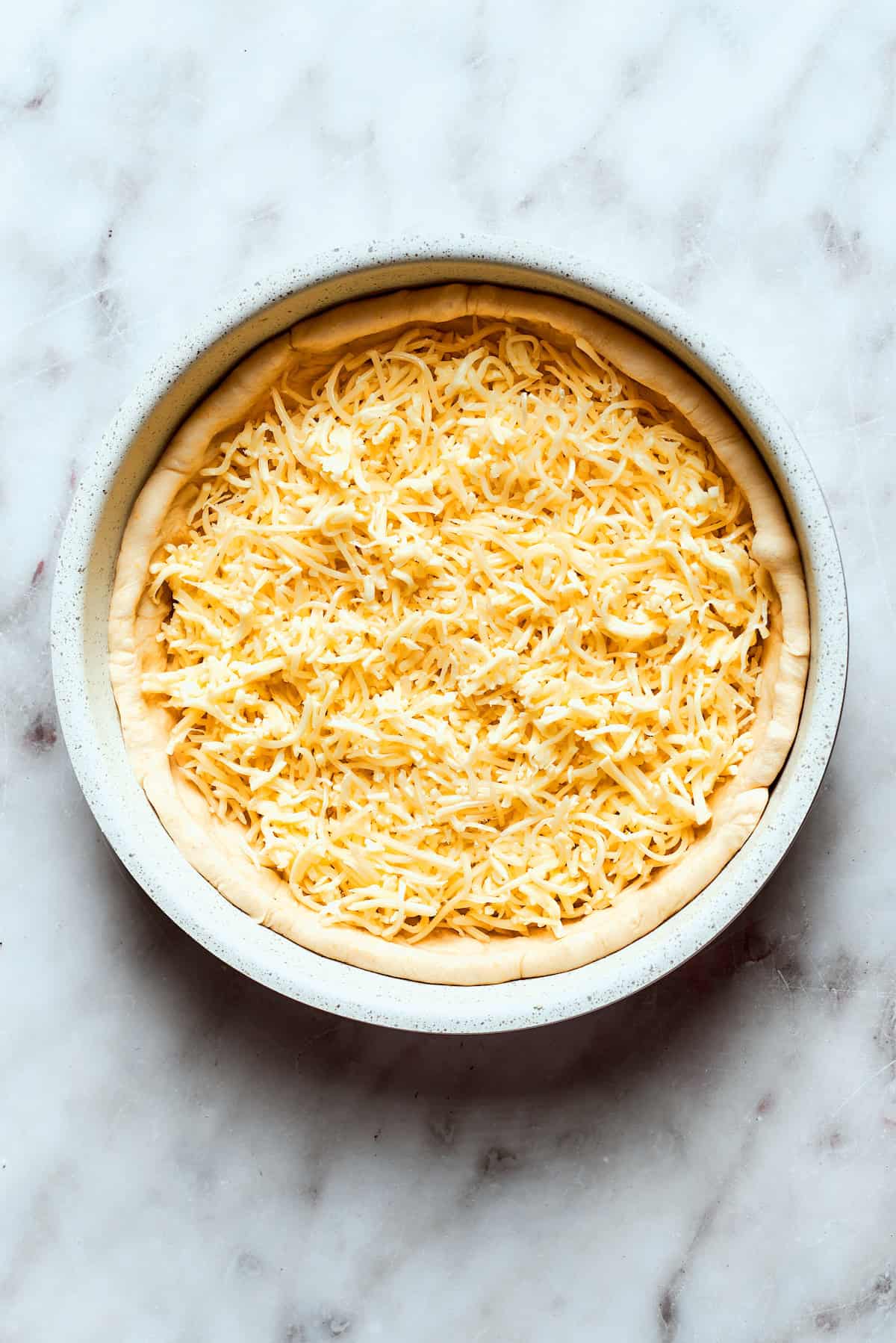 A generous layer of shredded mozzarella and Edam cheese is spread over the deep dish pizza dough.