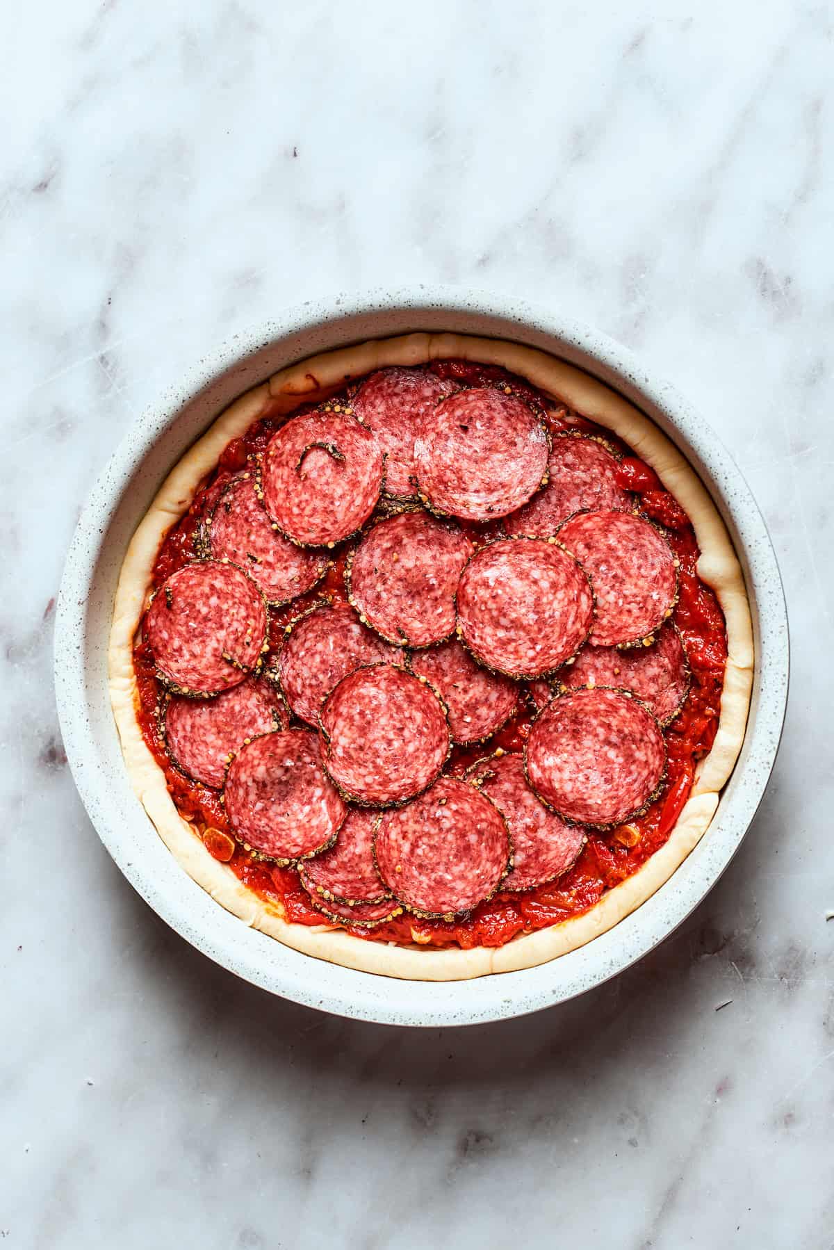 Sliced pepperoni pieces are carefully arranged over the deep dish pizza's top layer.