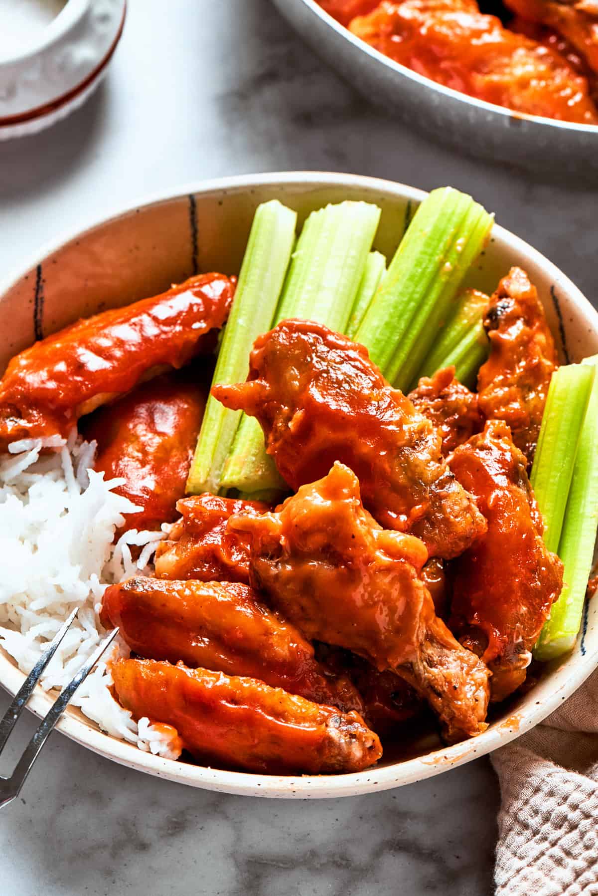 Buffalo chicken wings served in a bowl with celery sticks and rice.