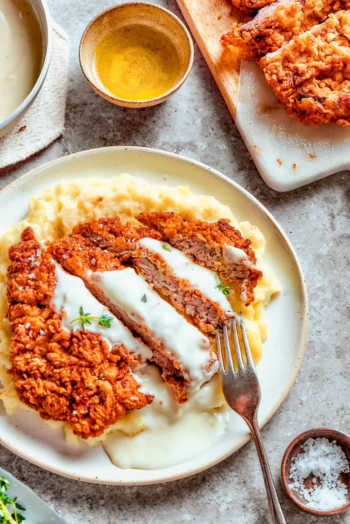 Sliced chicken fried steak served over mashed potatoes, and a fork is resting on top of the meat.