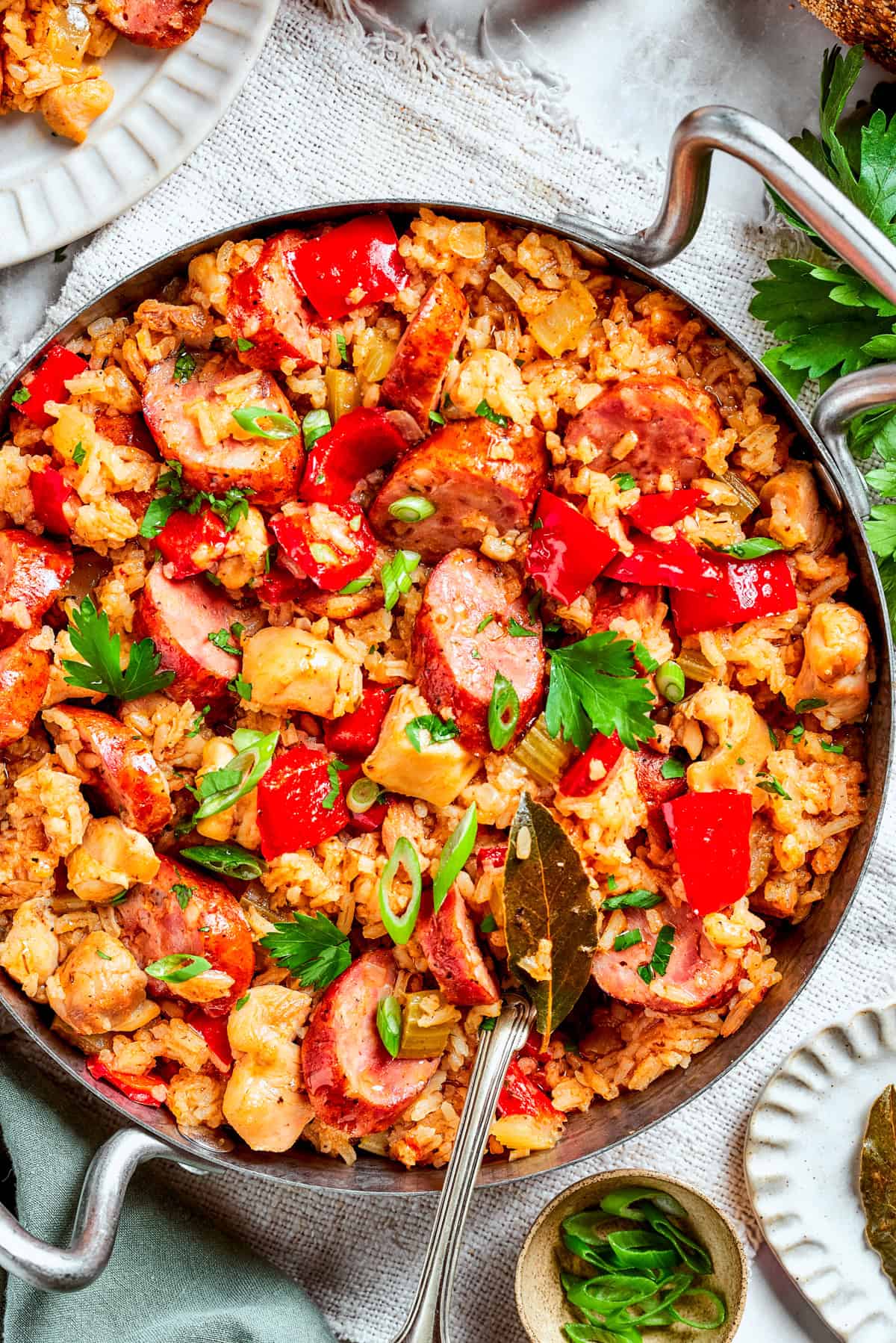 Image of a pan with jambalaya featuring a bed of rice topped with chicken bites, sliced sausages, and diced red bell peppers.