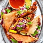 Chicken wonton tacos arranged on an oval platter with a bowl of sauce set right next to the tacos.