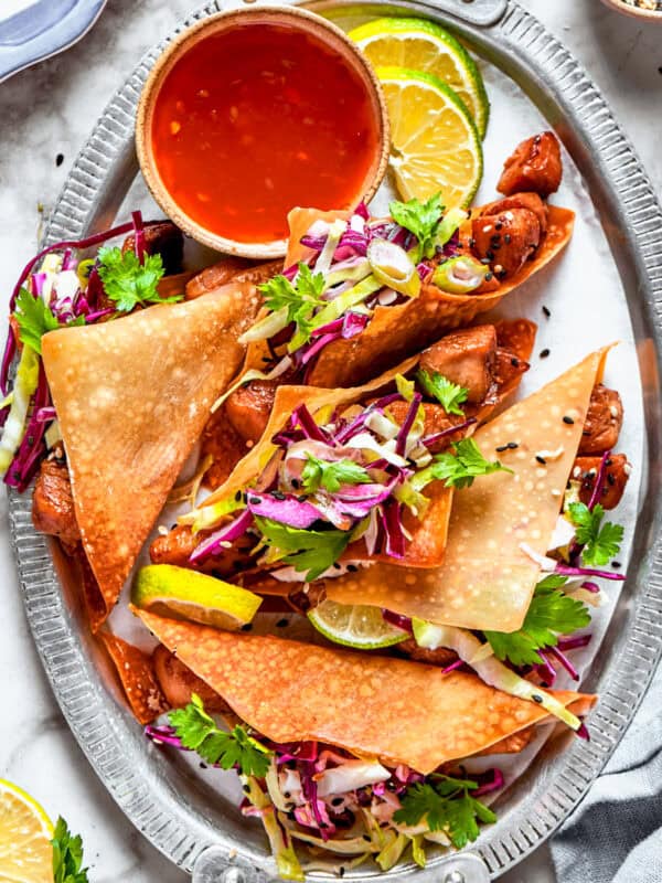 Chicken wonton tacos arranged on an oval platter with a bowl of sauce set right next to the tacos.