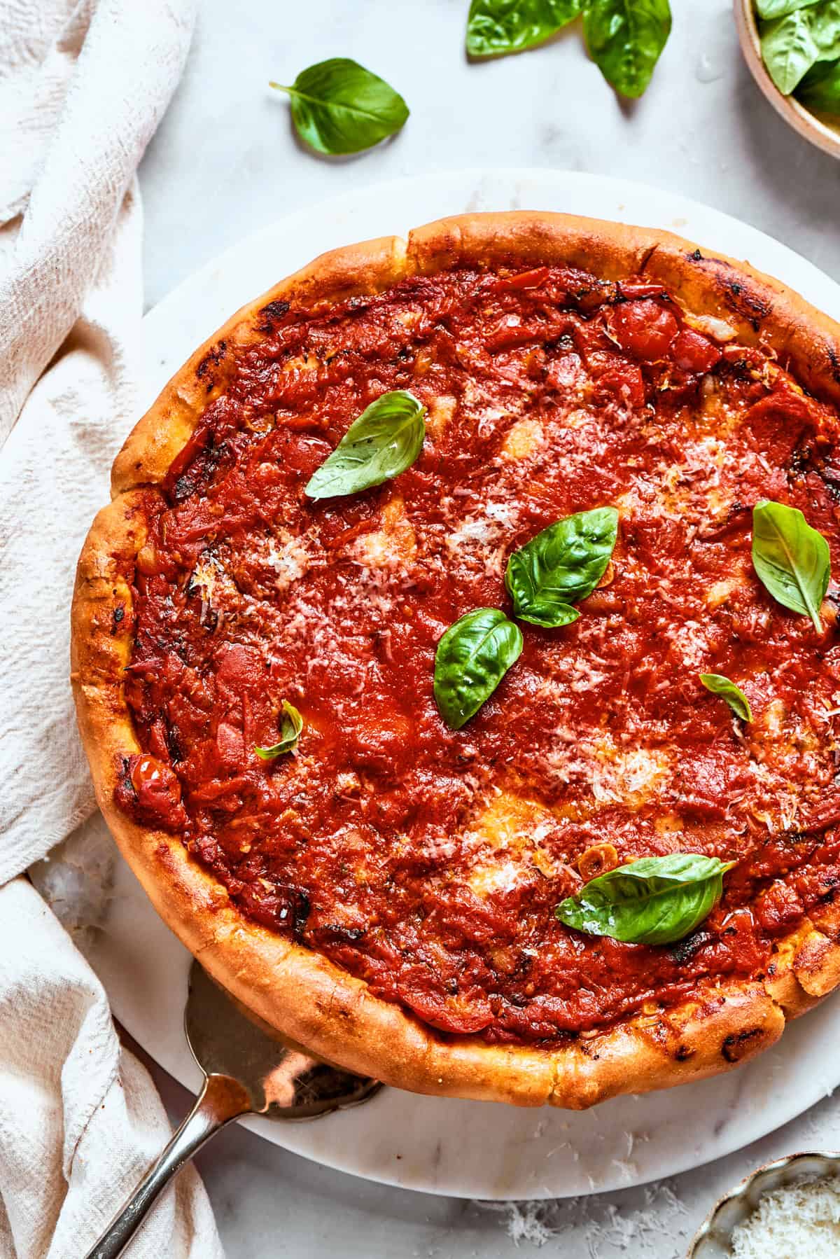 Overhead image of pizza topped with tomato sauce and garnished with fresh basil leaves.