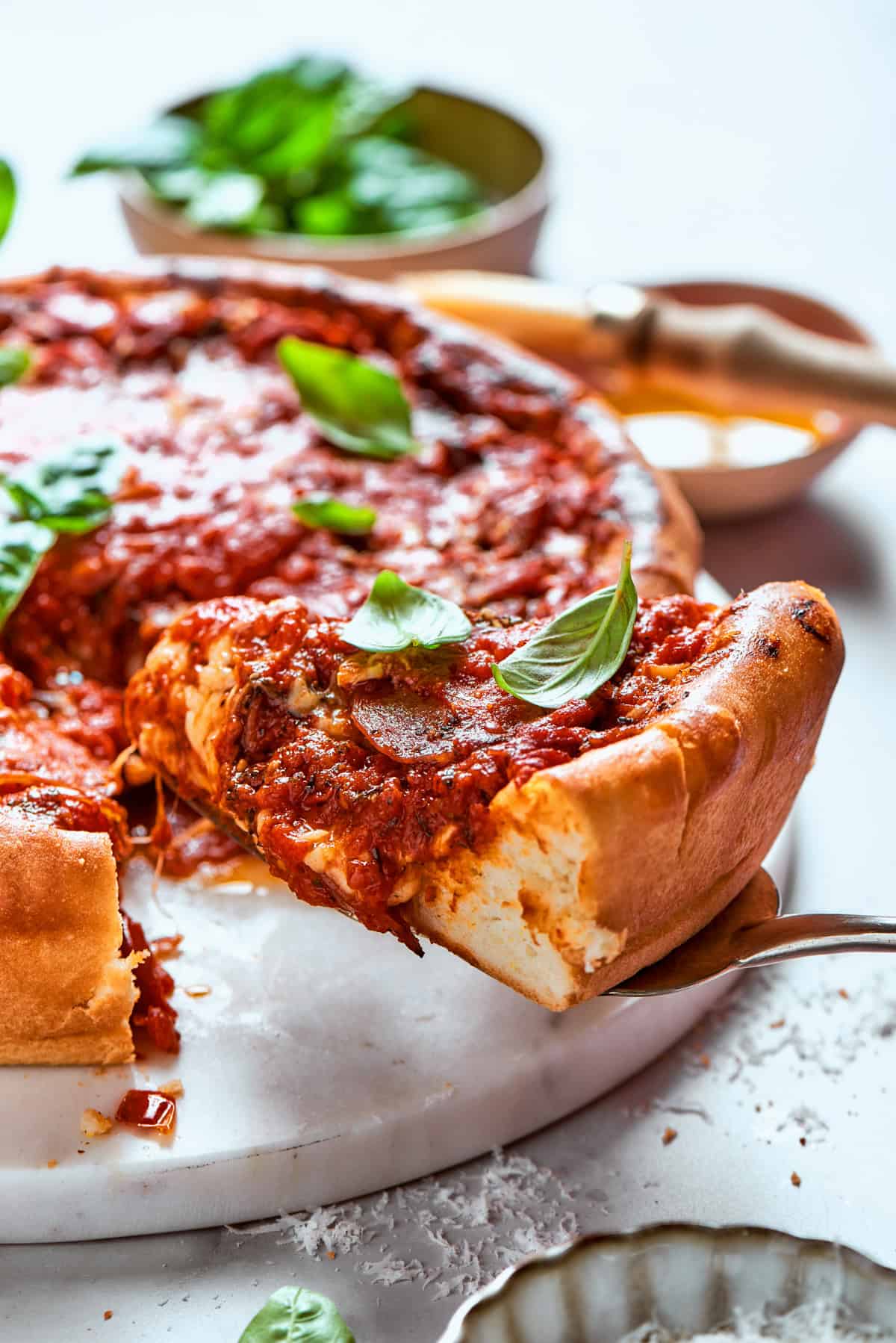 Serving spoon lifting out a slice of deep dish pizza.