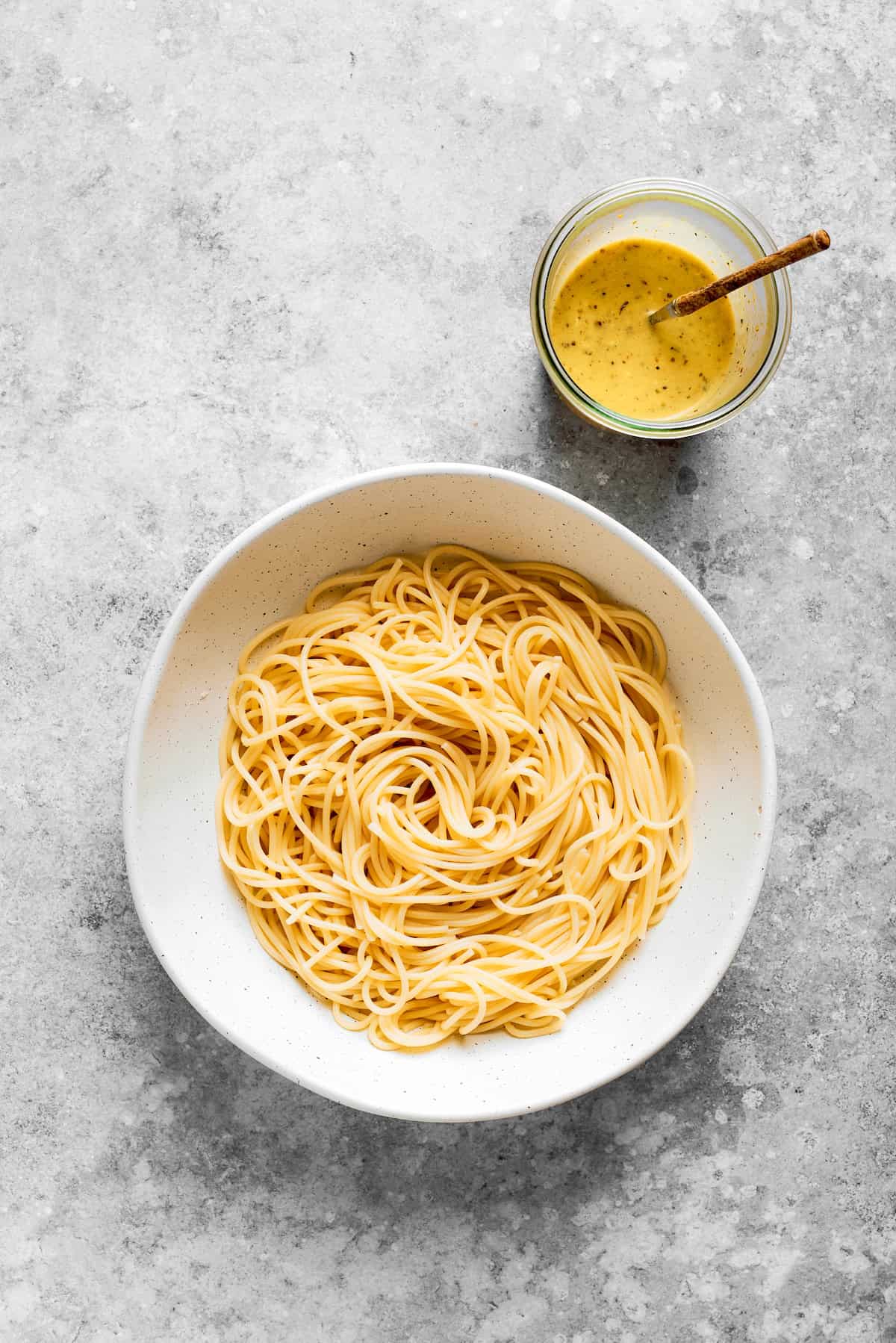 The spaghetti is placed in a bowl with the dressing next to it.