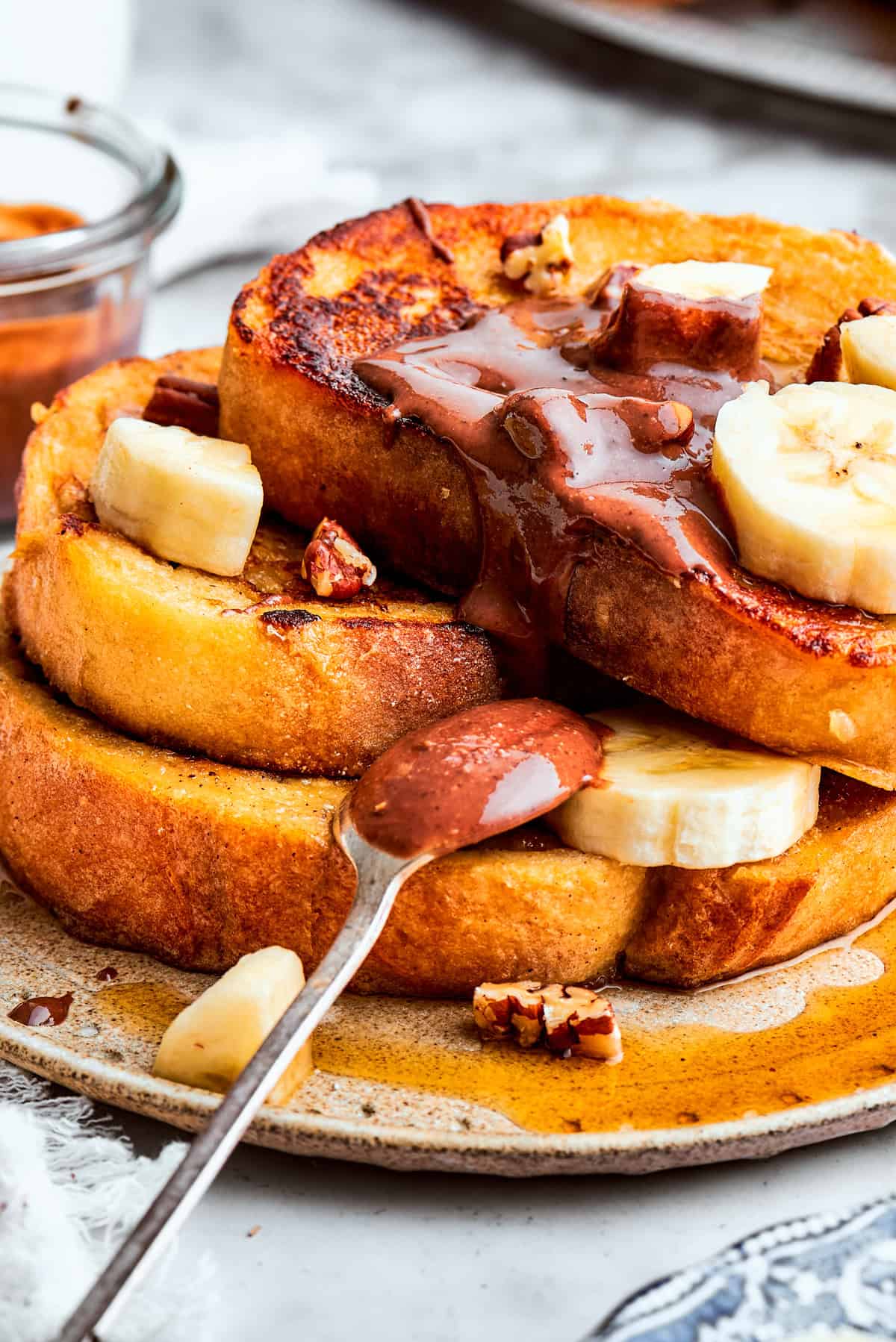 Close-up of a stack of French toast garnished with slices of banana and chocolate spread.