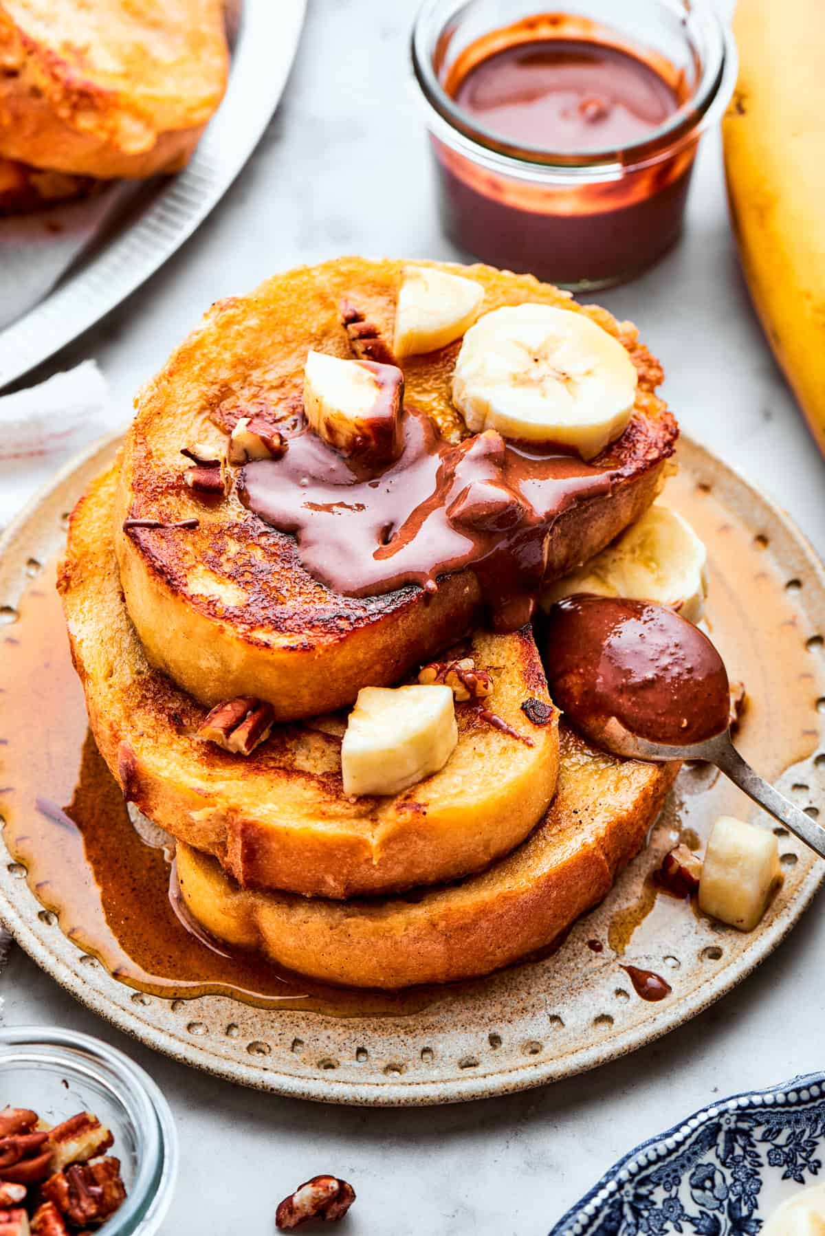 Three slices of French toast are stacked on top of each other on a plate and topped with banana slices and Nutella.