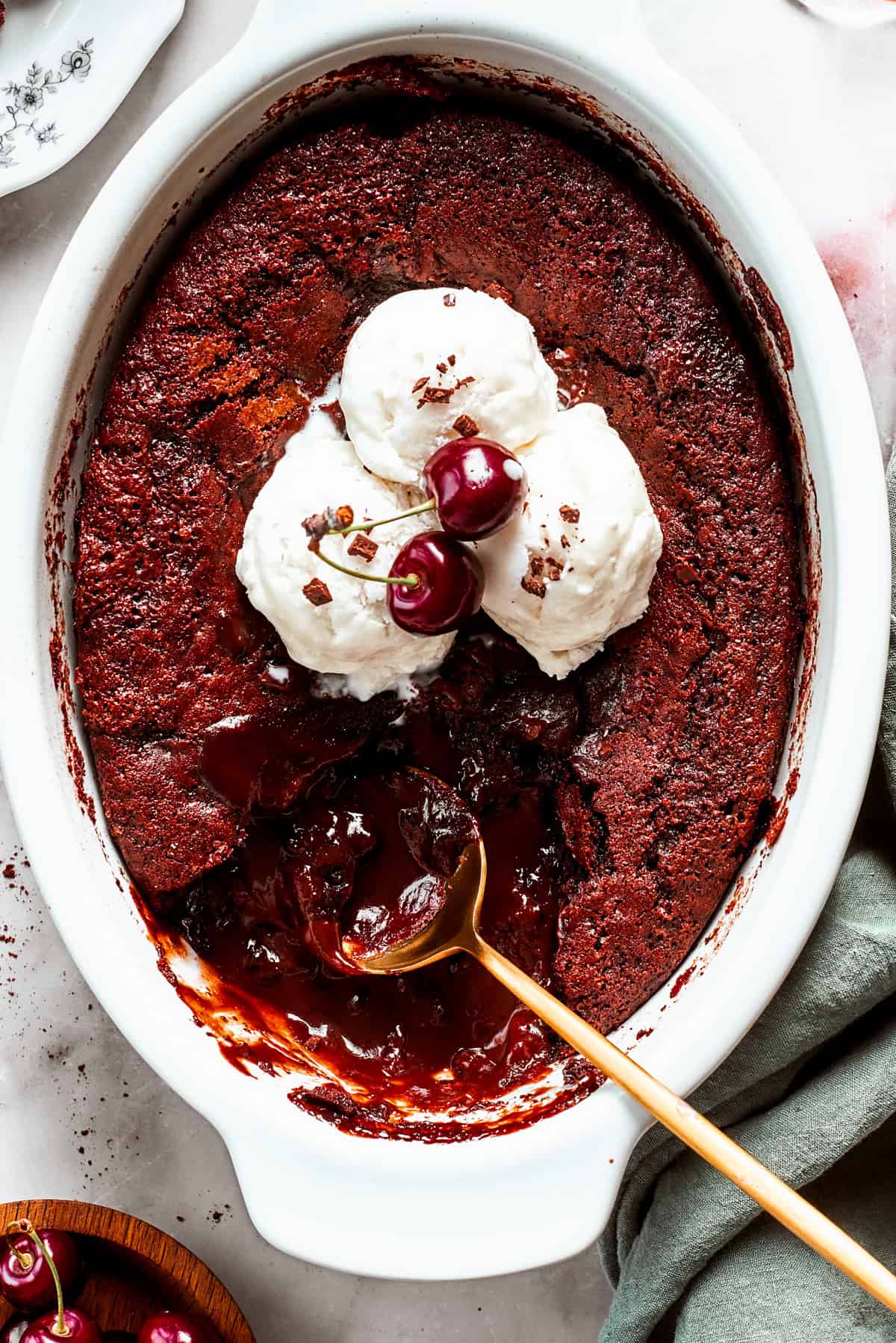 An oval casserole dish with chocolate pudding cake topped with vanilla ice cream, with a spoon set in the pudding.