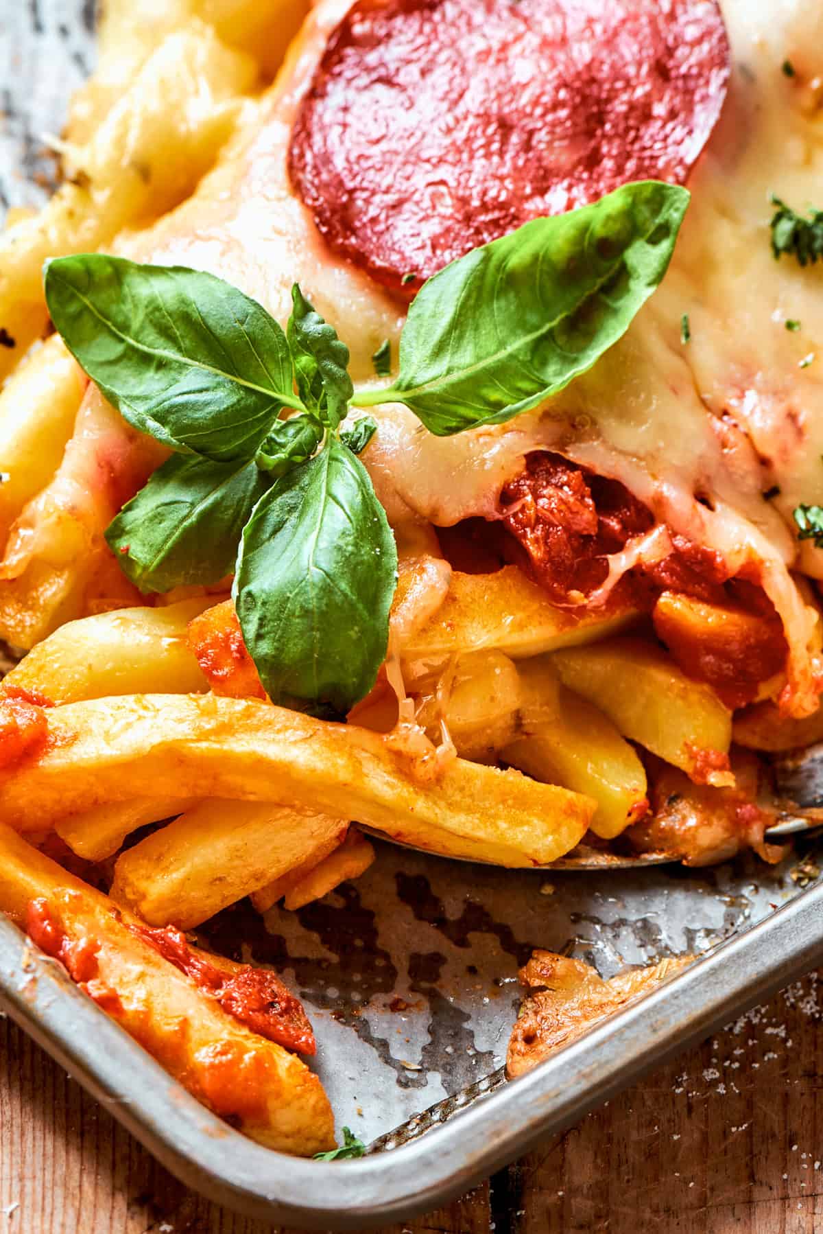 Close-up image of baked french fries garnished with fresh basil leaves.