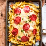 A baking tray with french fries topped with melted cheese and pepperoni.