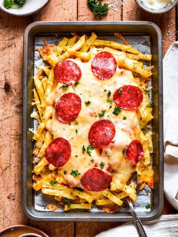 A baking tray with french fries topped with melted cheese and pepperoni.