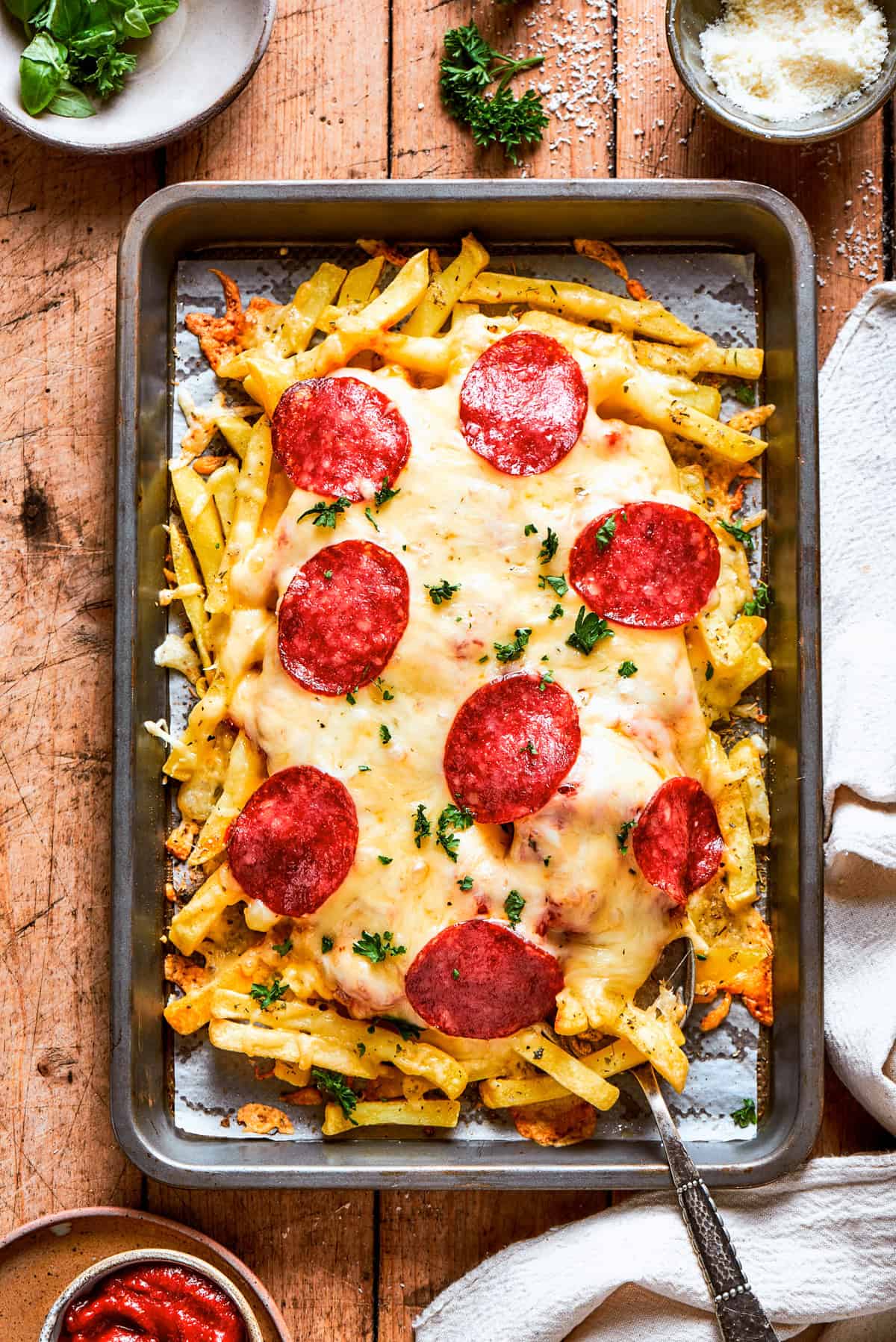 A baking tray with french fries topped with melted cheese and pepperoni.