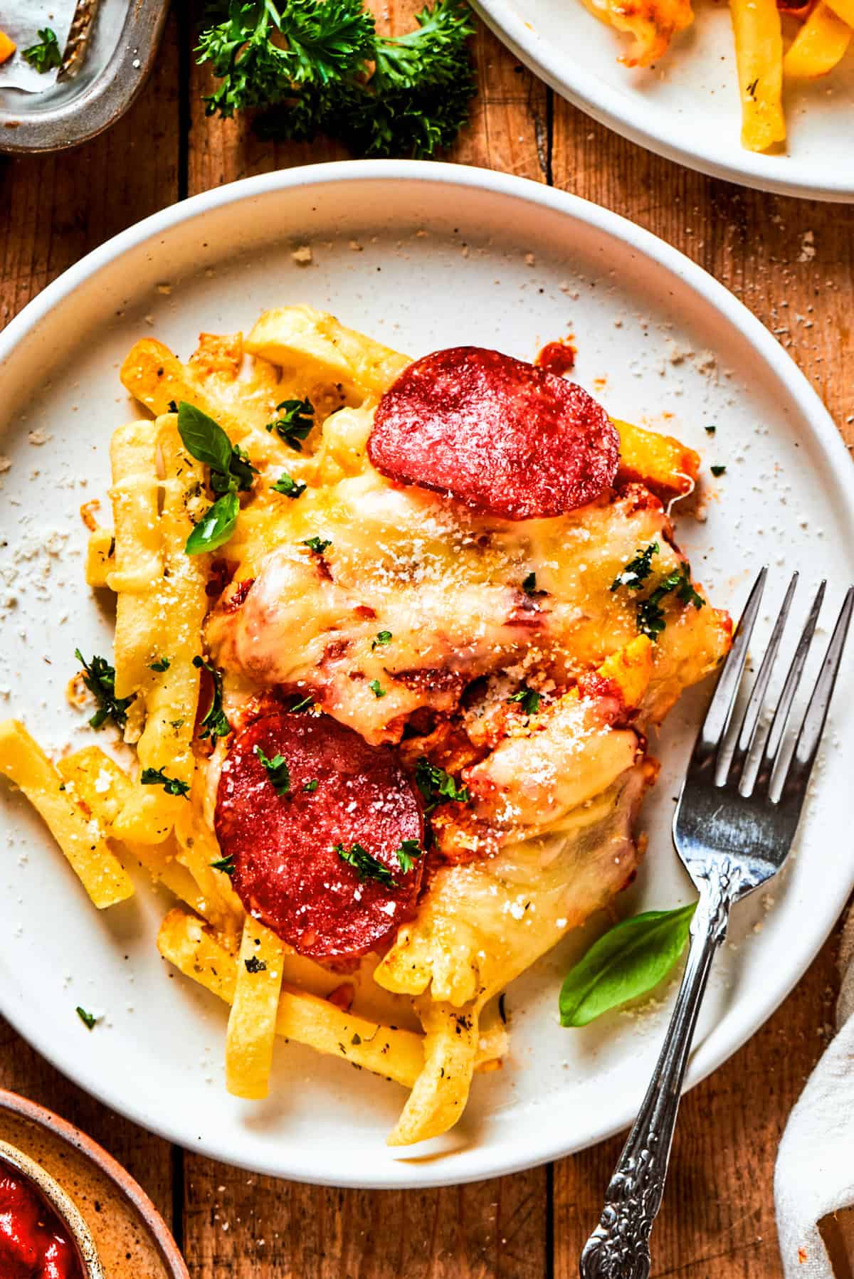 Pizza fries served on a dinner plate with a fork set next to the fries.