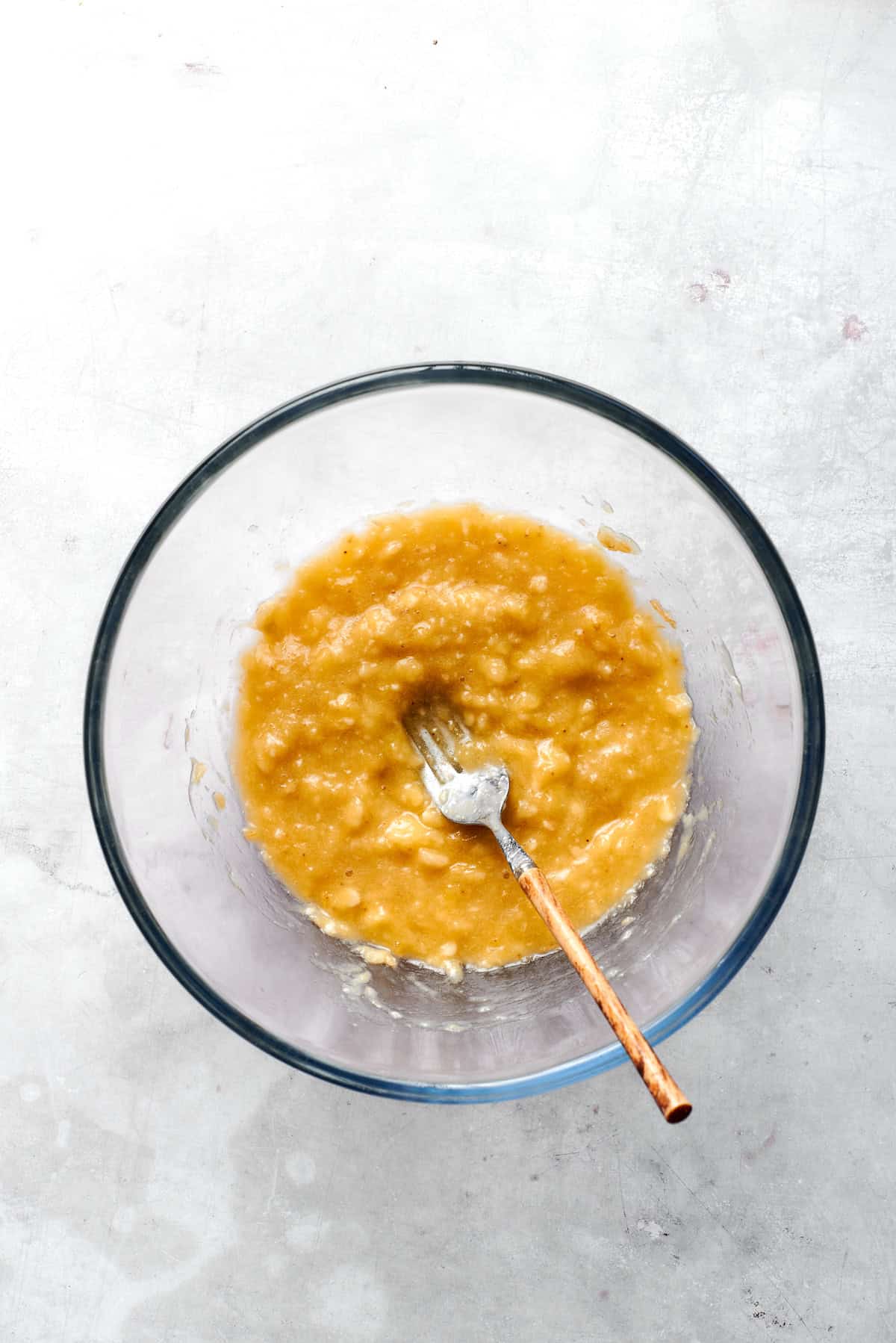 Bananas are mashed with a fork in a bowl.