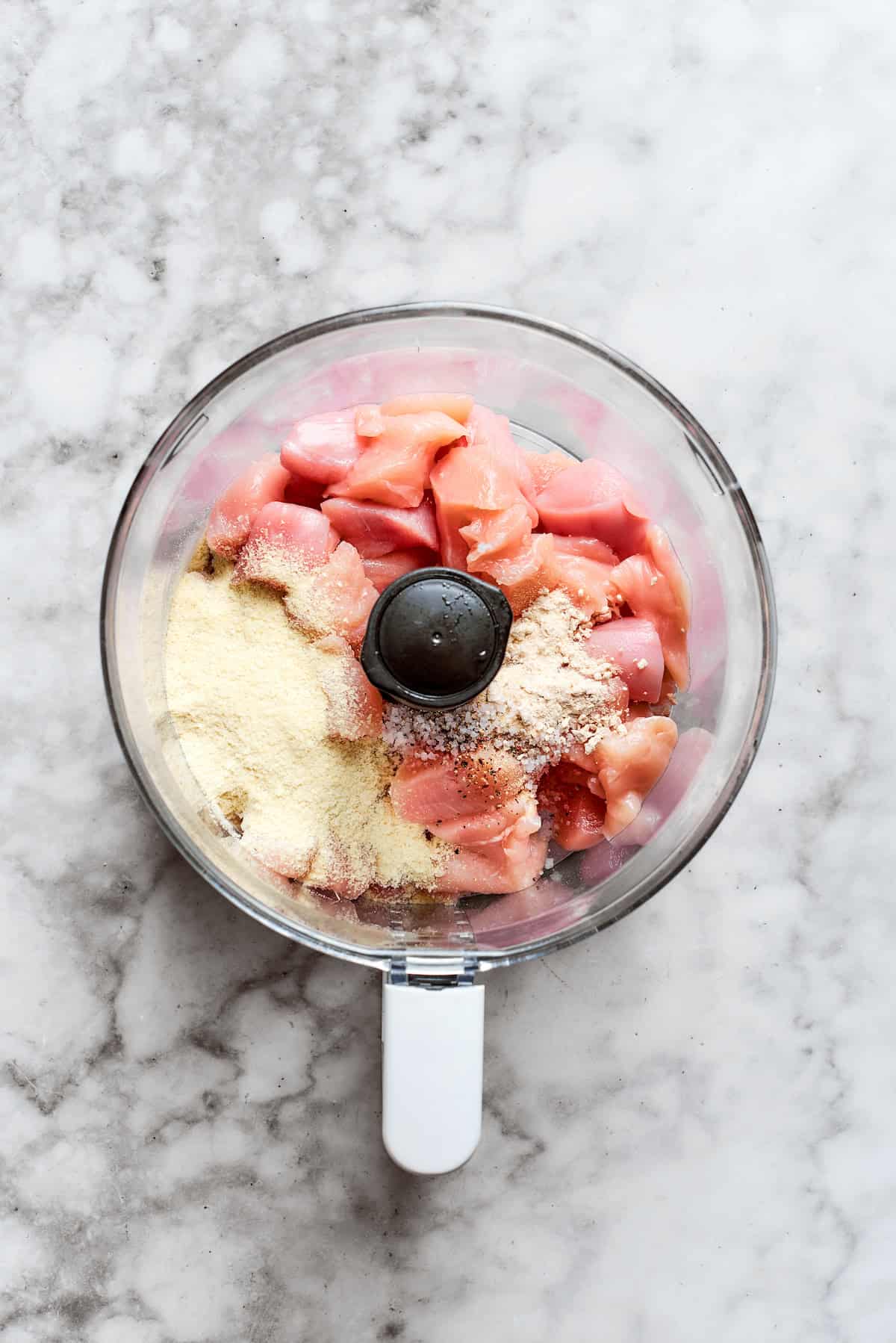 Chicken pieces and spices are added to a food processor.