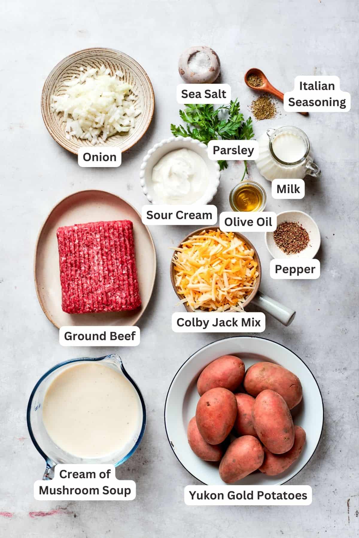 Ingredients for hamburger potato casserole: ground beef, cheese mix, onion, sour cream, salt, pepper, milk, seasoning, mushroom soup, potatoes.