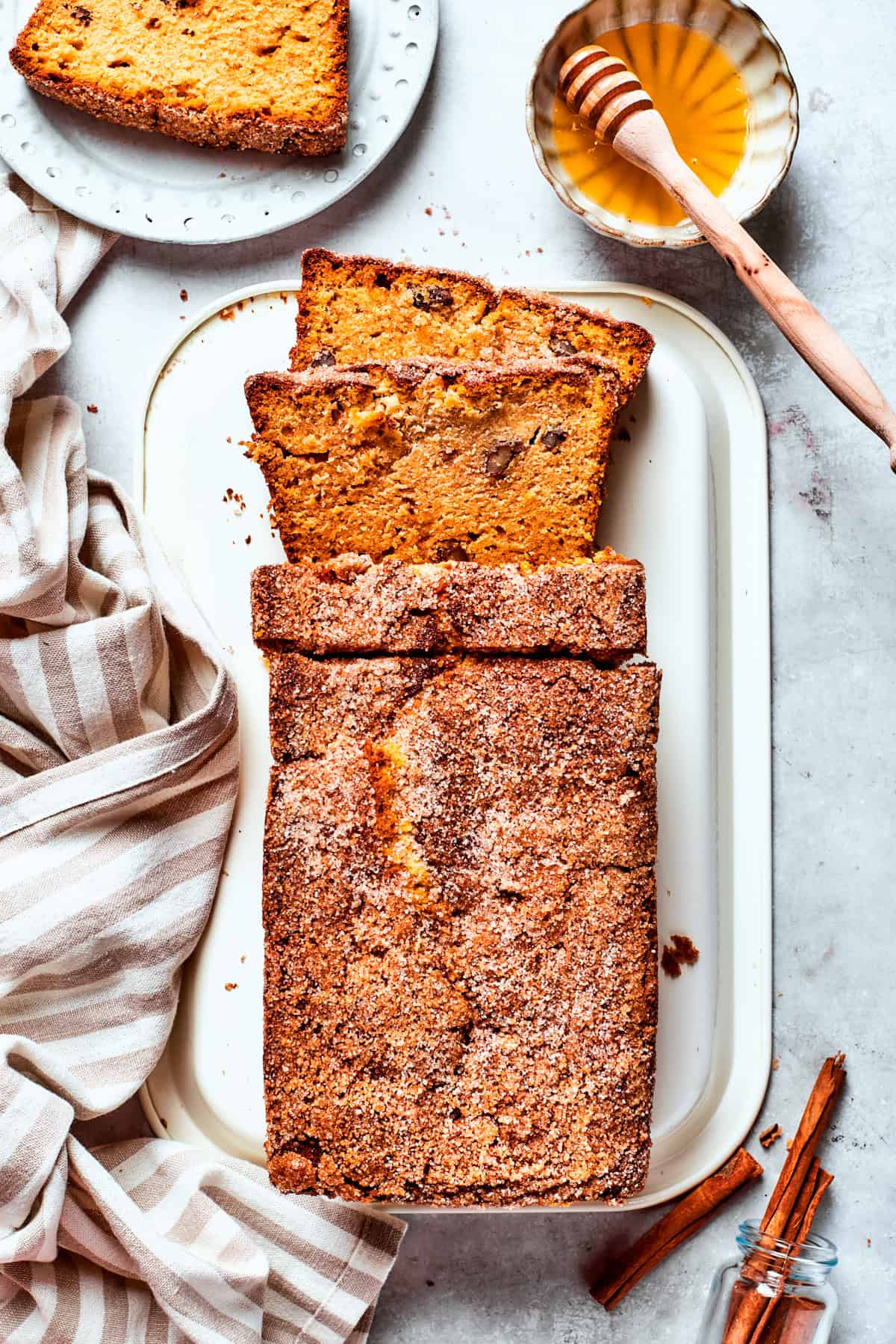 A serving platter with a loaf of Amish friendship bread with a slice cut out next to a bowl of honey.